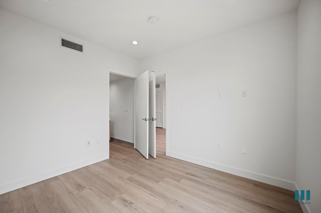 A room with a white wall and a wooden floor with a doorway.