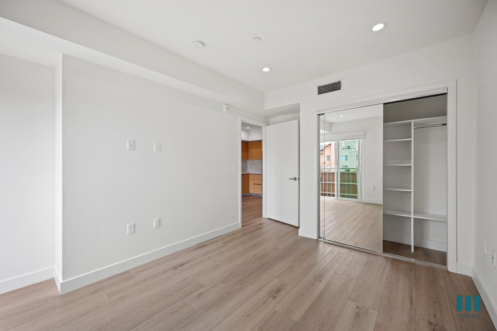 A room with white walls and wooden flooring with a doorway leading to another room.