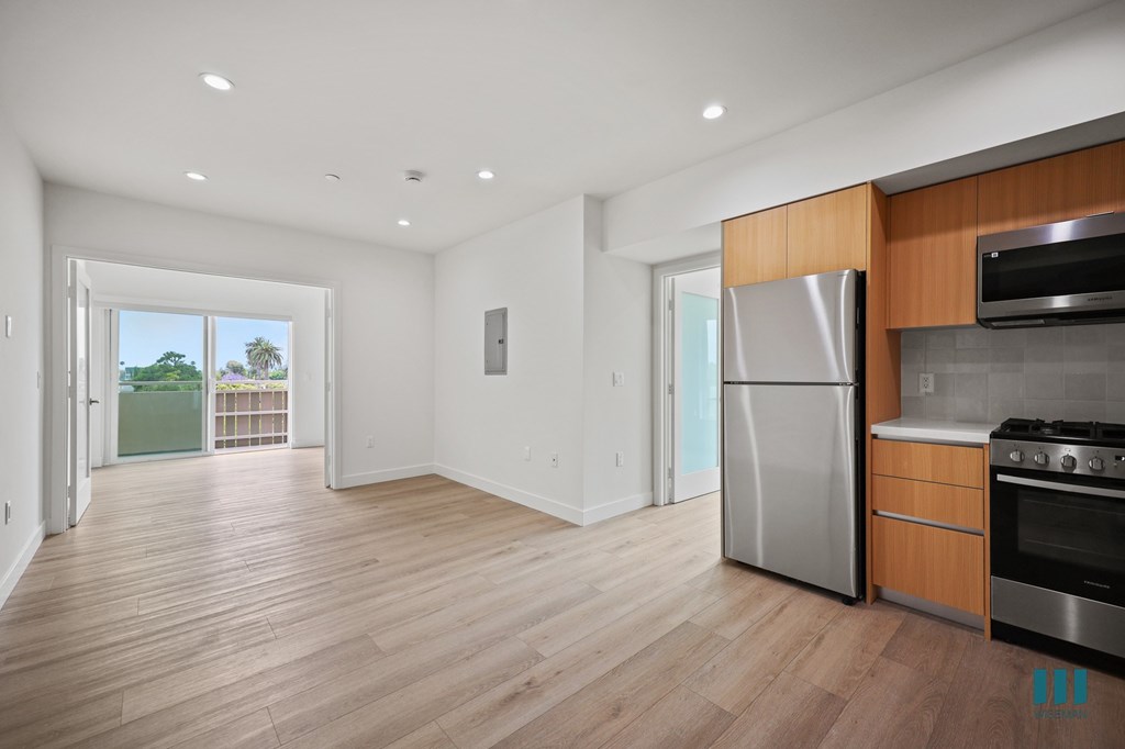 A kitchen with a stainless steel refrigerator and oven, and wooden flooring.