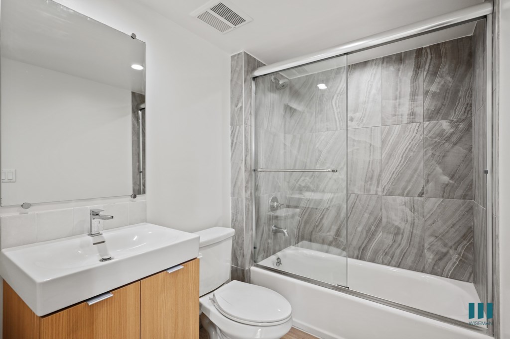 A modern bathroom with a marble shower wall and a white sink.