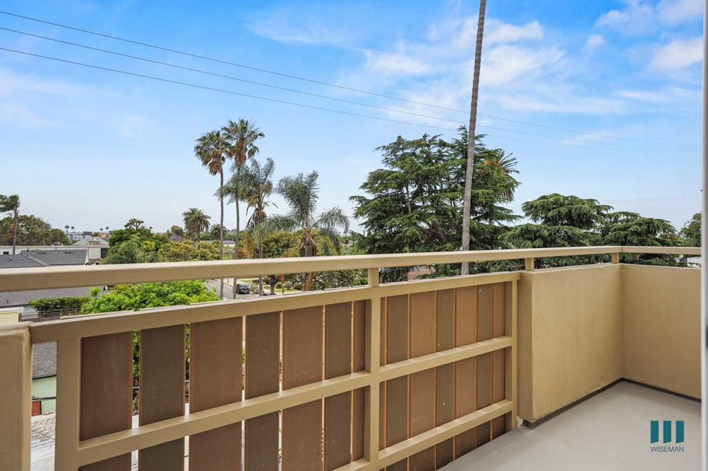 A balcony with a wooden railing overlooks a residential area with palm trees.