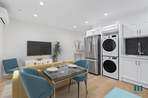 a living room with a table and chairs and a kitchen with washer and dry