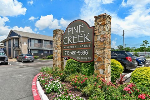 A sign for Pine Creek Apartment Homes stands in front of a building.