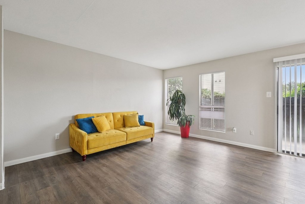 A yellow couch with blue pillows sits in a room with a plant in a red pot.