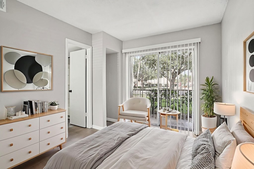 A bedroom with a large bed, a chair, a table, and a window with a view of trees.