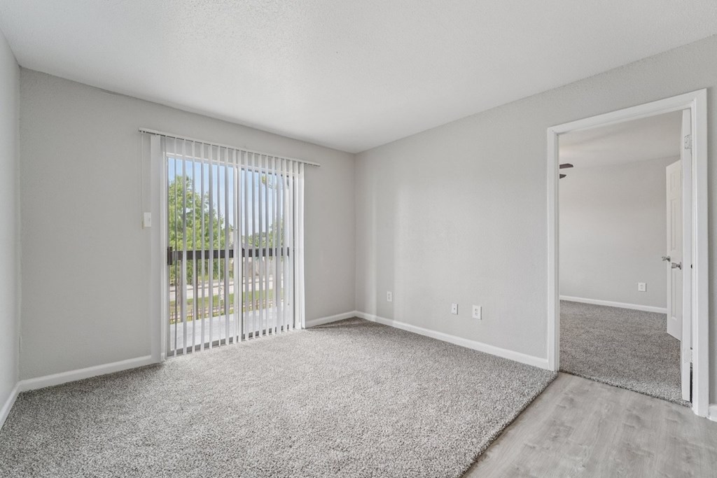 A room with a carpeted floor and a sliding glass door leading to a balcony.