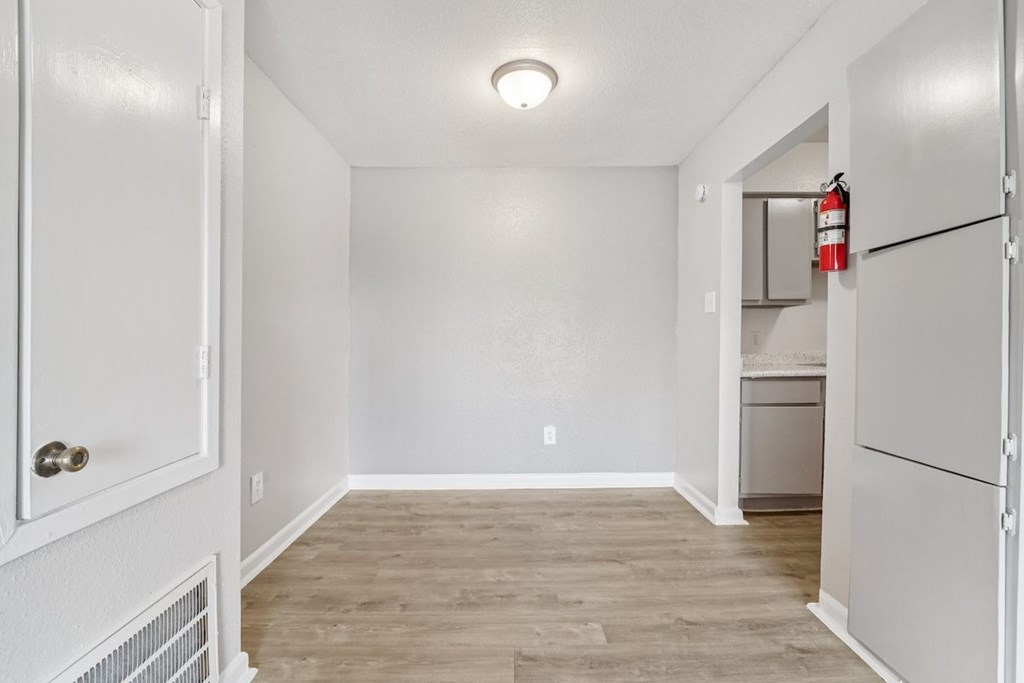 A white door opens to a room with a wood floor and a white wall.