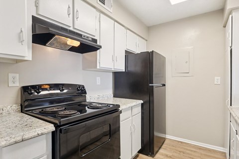 A black stove and refrigerator in a kitchen with white cabinets.