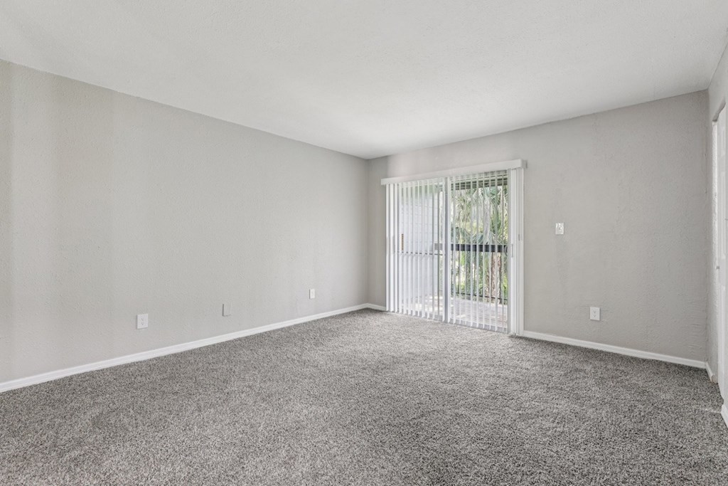 A spacious room with a carpeted floor and a sliding glass door leading to a balcony.