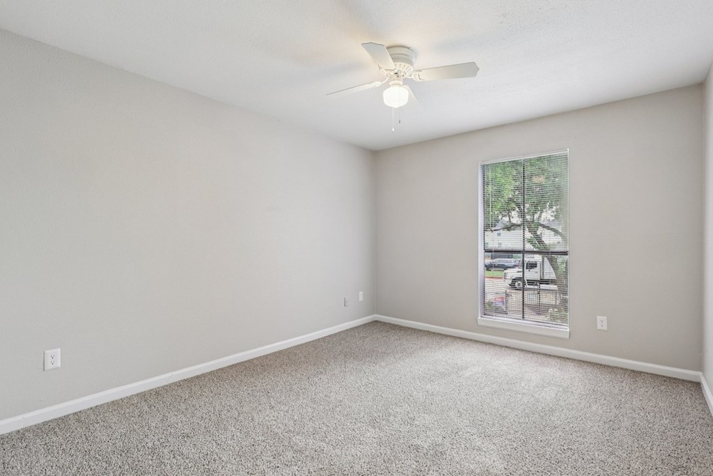 A room with a ceiling fan and a window showing a parking lot outside.