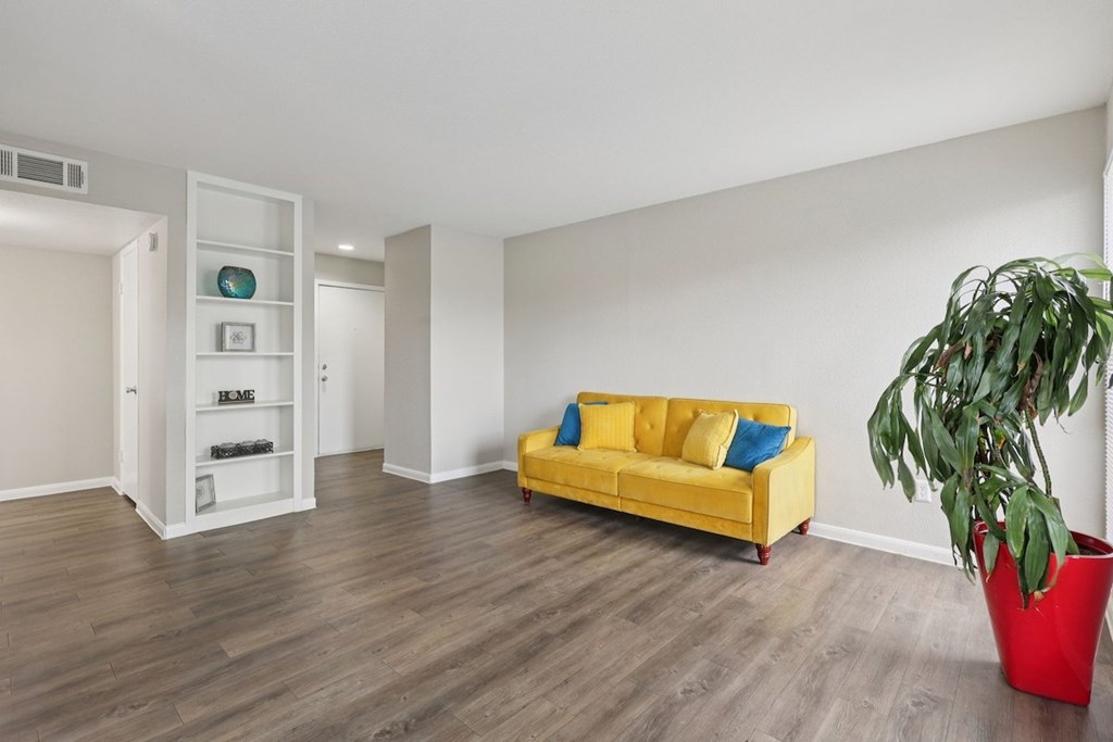 A living room with a yellow couch and a red planter.