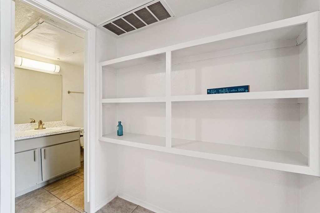 A white bathroom with a white shelving unit and a mirror.