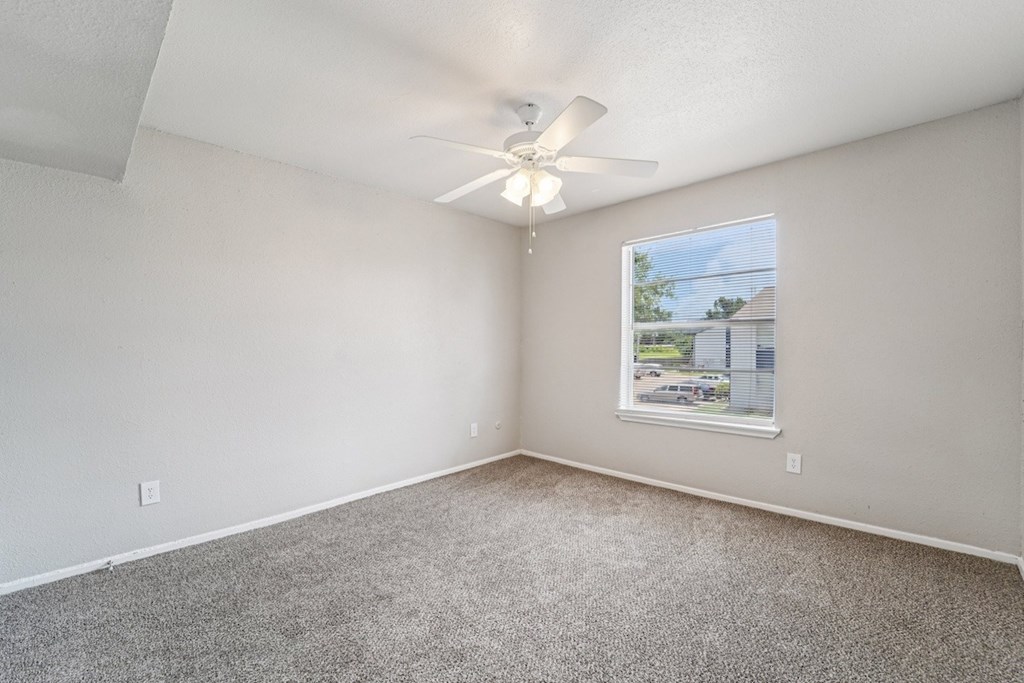 A room with a ceiling fan and a window showing a view of a house.