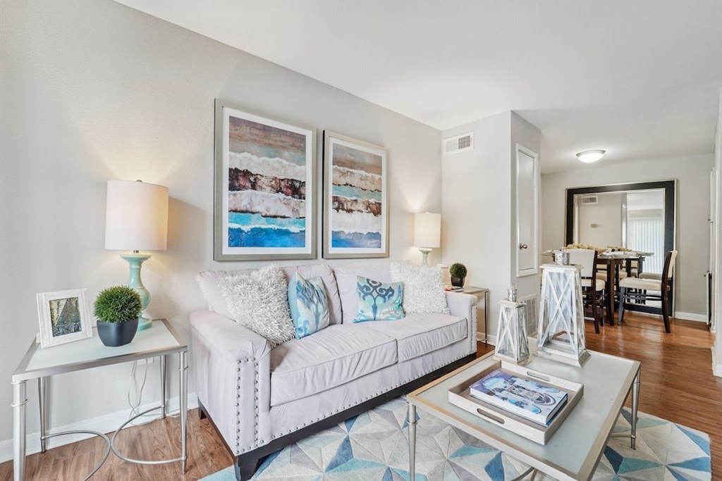 A living room with a white couch, a small table with a plant, and a painting on the wall.