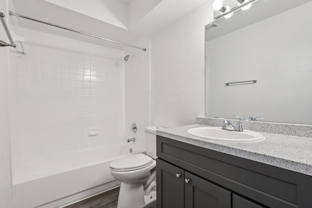 A white toilet sits in a bathroom with a white tub and a sink.