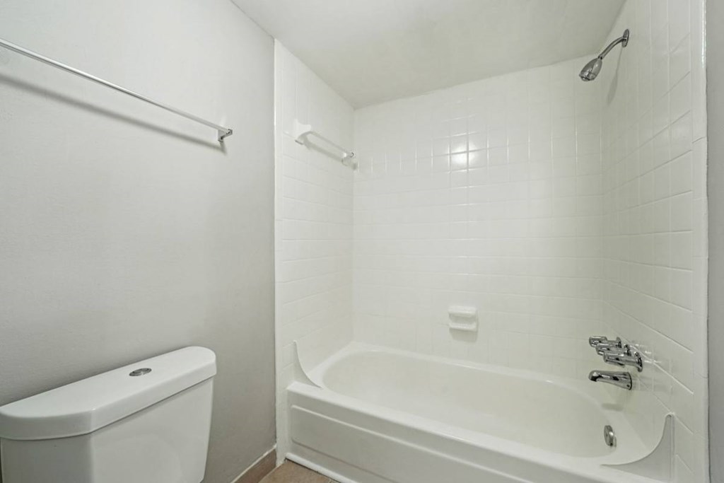 A white bathroom with a toilet, bathtub, and shower.at Hills at Hoover Apartments, Hoover