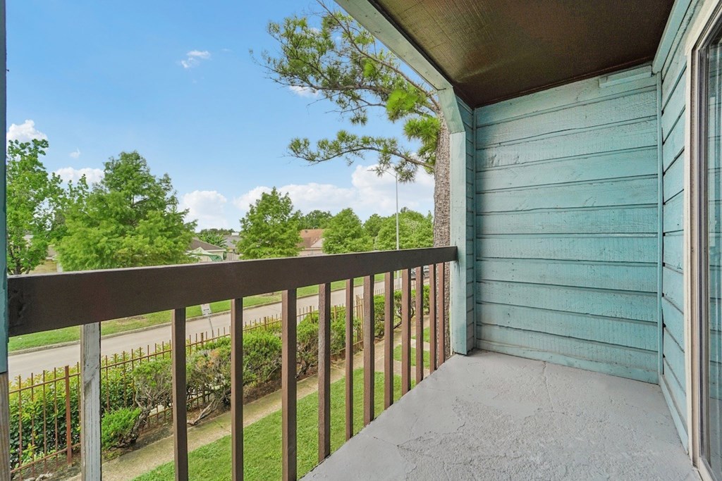 A balcony with a metal railing and a view of a green lawn and trees.