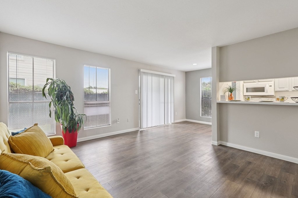 A living room with a yellow sofa and a kitchen area in the background.