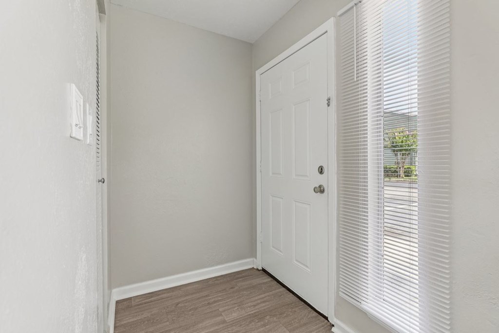A white door is in a room with a window covered by blinds.