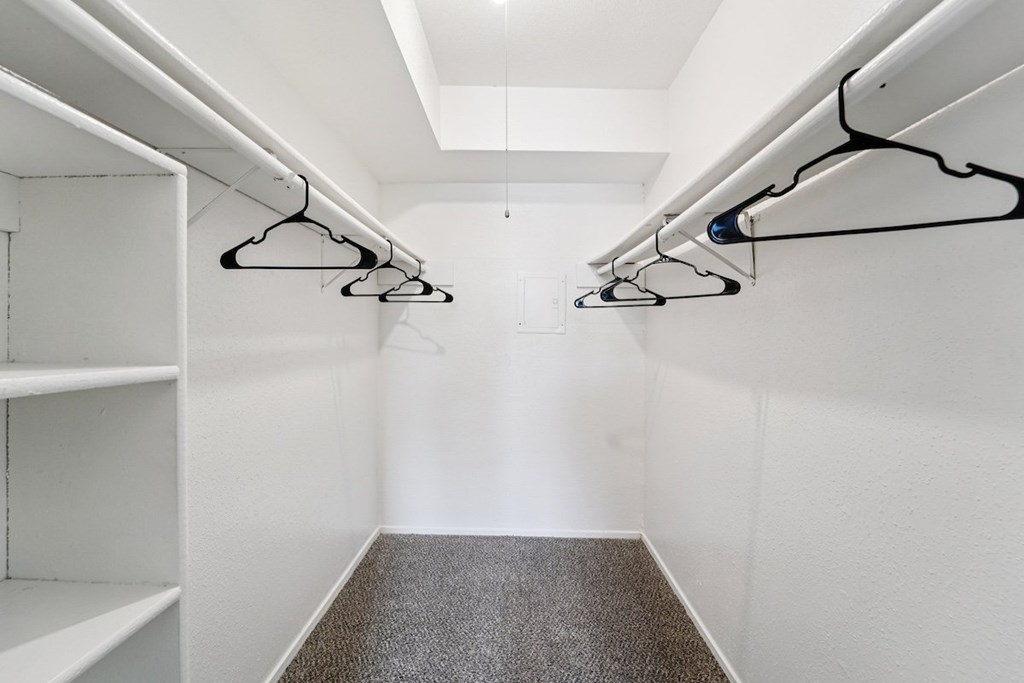 A walk-in closet with white shelves and black hangers.