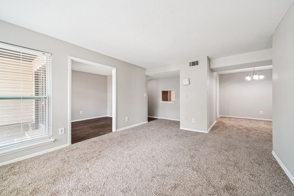 A spacious, empty room with a carpeted floor and a window with blinds.at Hills at Hoover Apartments, Hoover, 35216