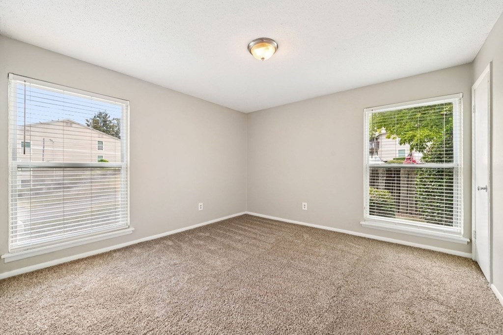 A room with carpeted floor, two windows with blinds, and a ceiling light.at Hills at Hoover Apartments, Hoover, AL 35216