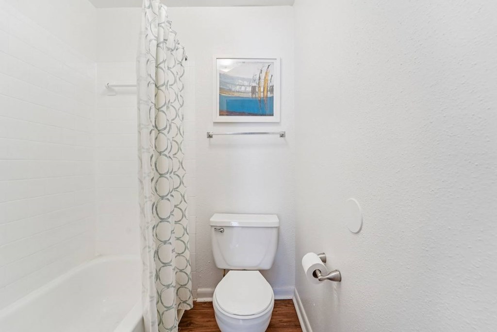 A white toilet sits in a small bathroom with a white shower curtain.