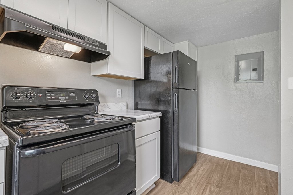 A black stove and oven in a kitchen with white cabinets and a black fridge.