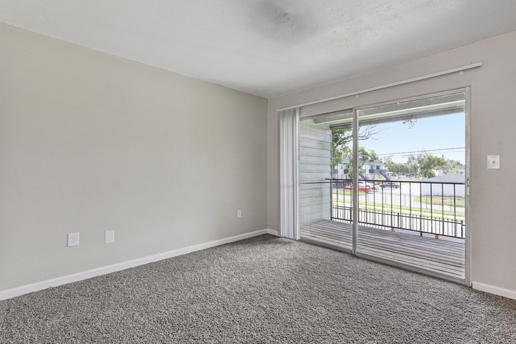 A room with a grey carpet and a sliding glass door leading to a balcony.