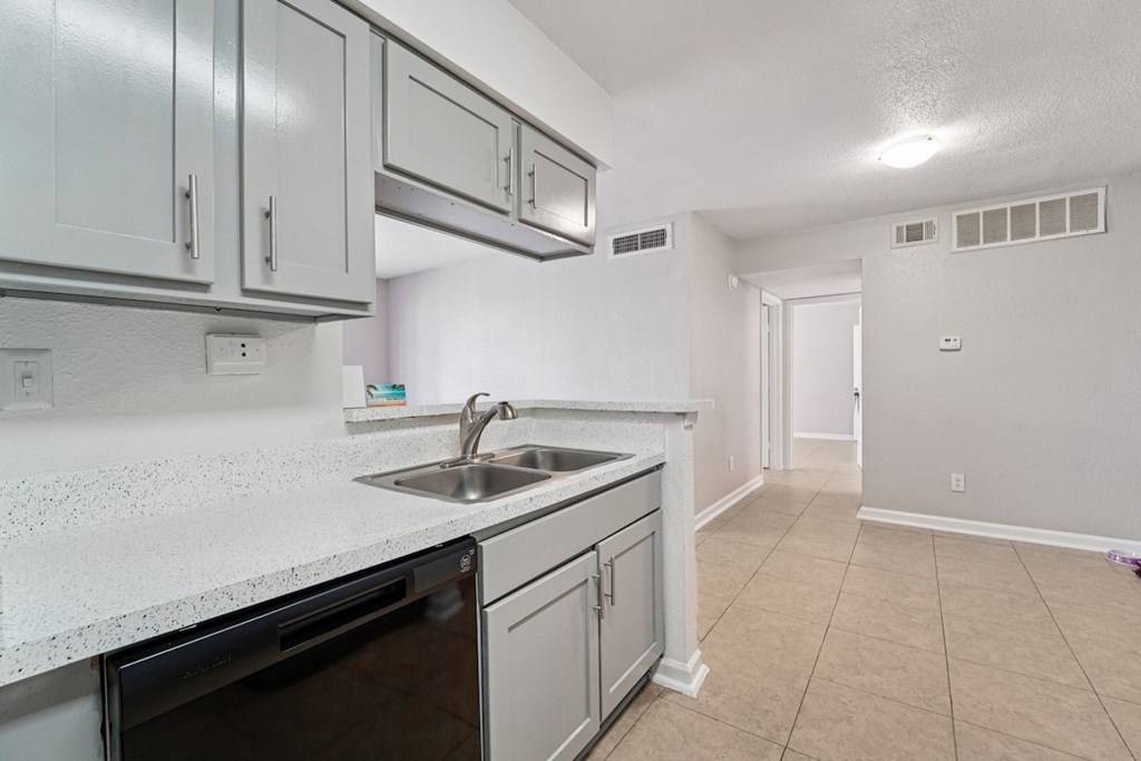 A kitchen with a black dishwasher and white cabinets.
