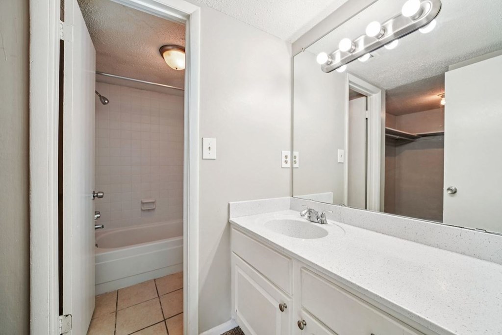 A white bathroom with a sink, mirror, and bathtub.at Hills at Hoover Apartments, Alabama