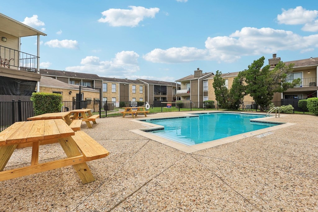 A pool surrounded by picnic tables and apartment buildings.