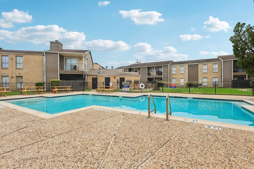 A swimming pool surrounded by a stone patio and apartment buildings.