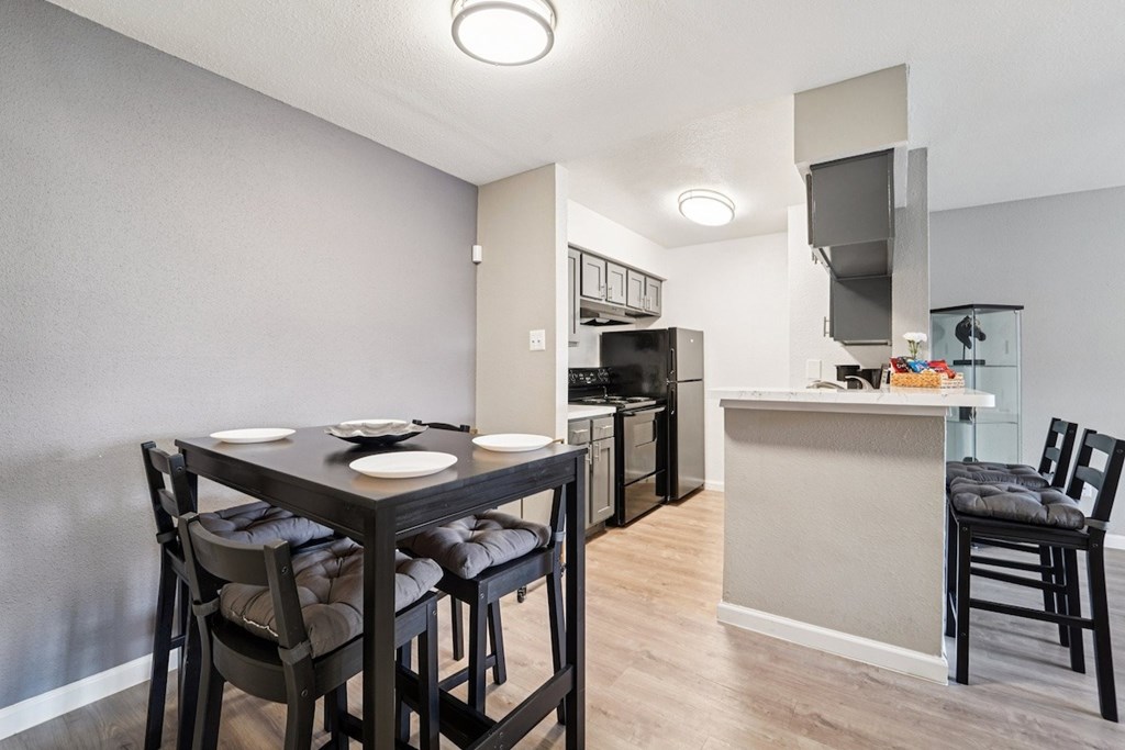 A kitchen with a table and chairs in the foreground and a counter with a sink and a microwave in the background.