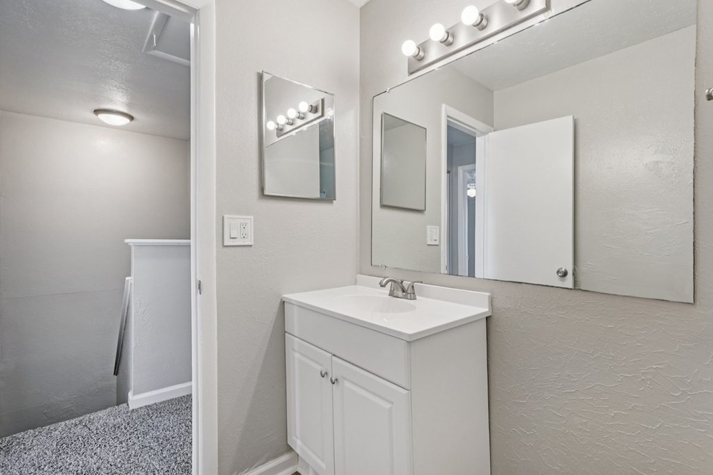 A white bathroom with a sink, mirror, and lighting.