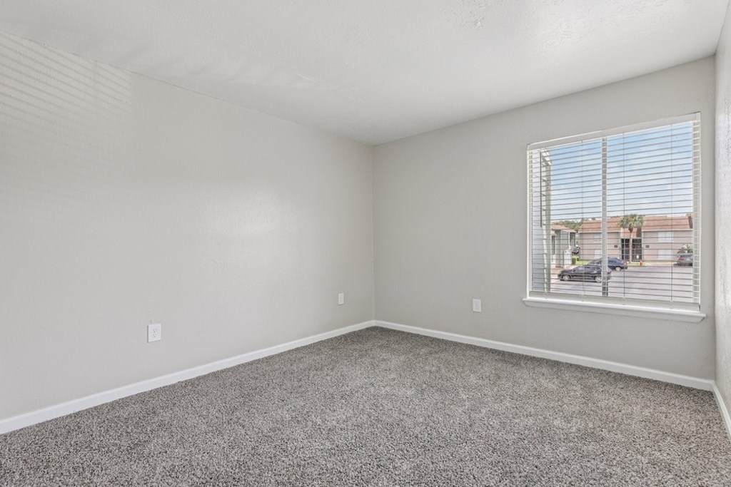 A room with a carpeted floor and a window with blinds.