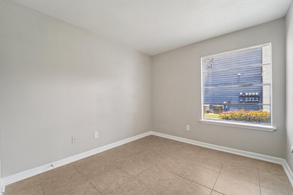 A room with a window showing a view of a building and some plants outside.