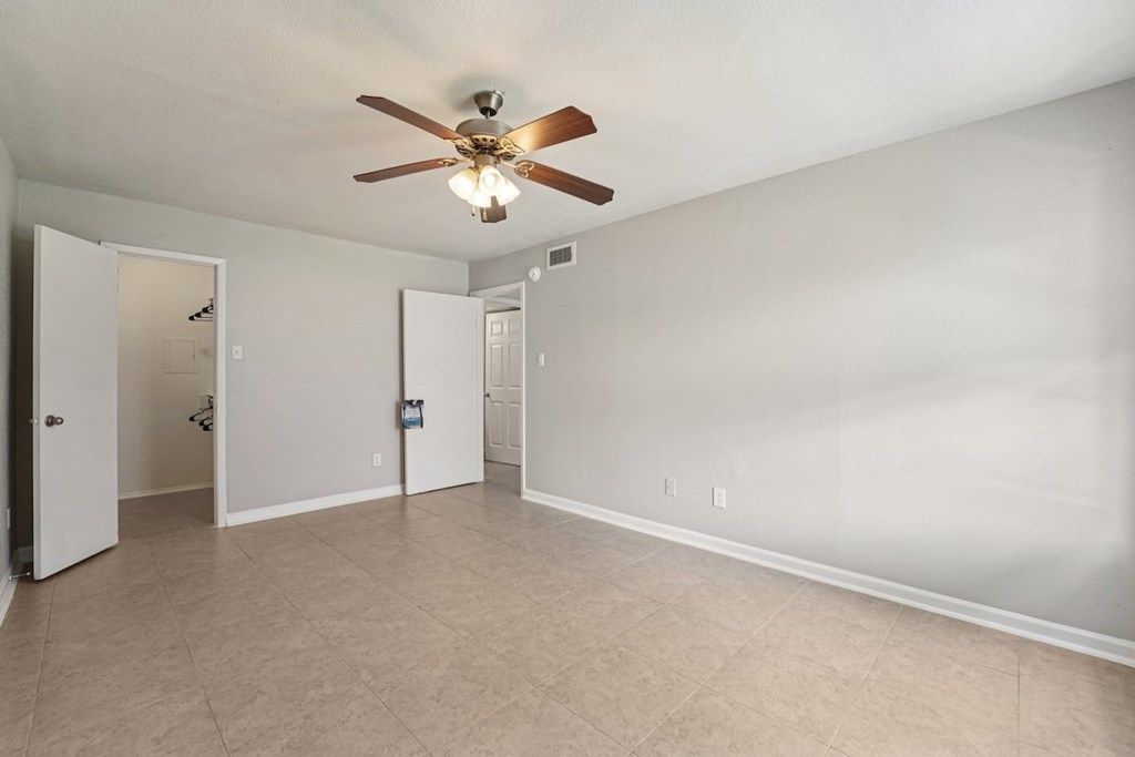 A room with a ceiling fan and beige carpeting.