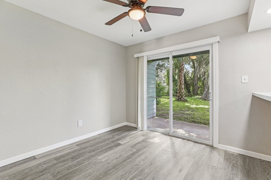 A room with a ceiling fan and sliding glass doors leading to a backyard.