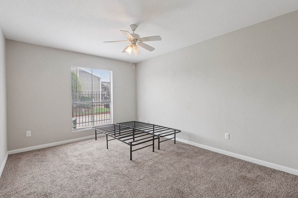 A room with a fan, carpet, and a metal bed frame.