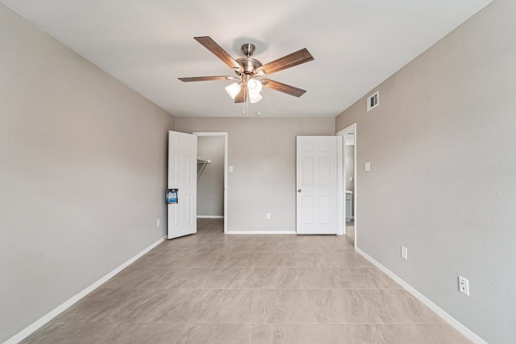 A room with a ceiling fan and light fixture, and a doorway leading to another room.