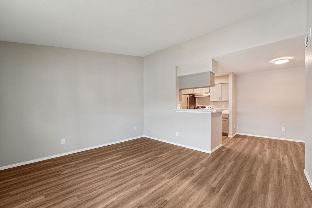 A room with wooden flooring and a kitchen area in the background.