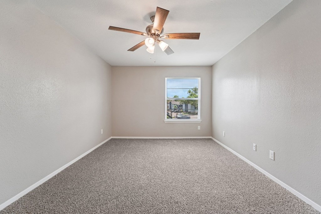 A room with a ceiling fan and a window showing a view of buildings outside.