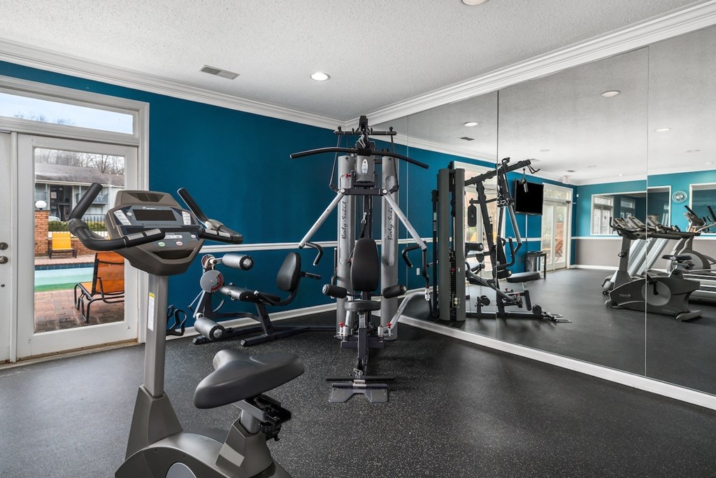 a gym with weights and cardio equipment in a home with blue walls and a window at Ascot Place Apartments, Birmingham Alabama