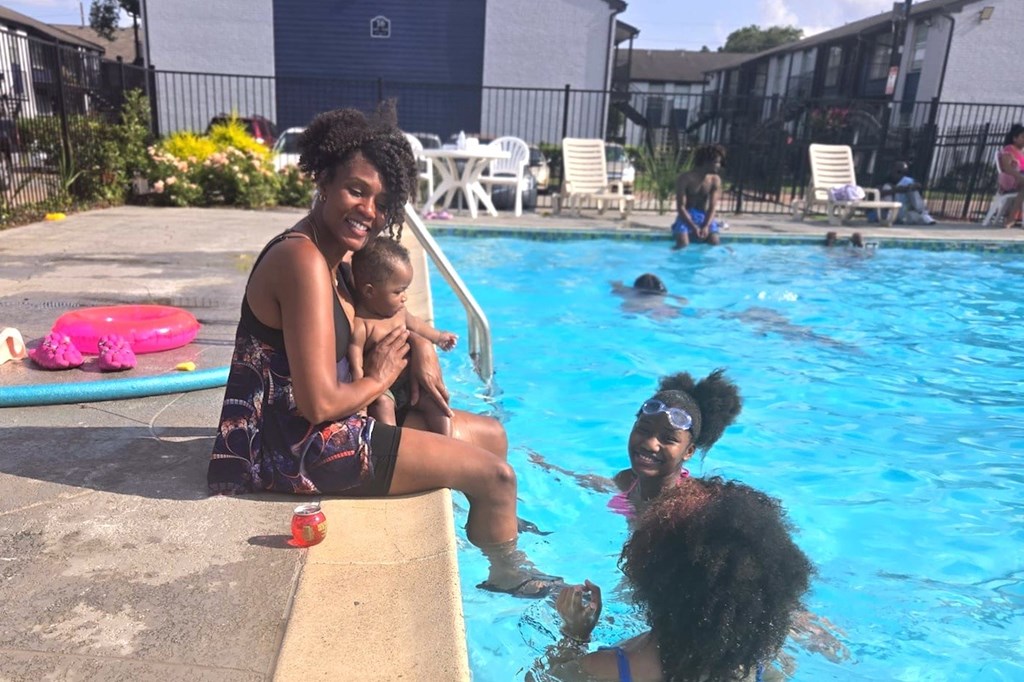 A woman holding a baby while sitting on the pool edge.