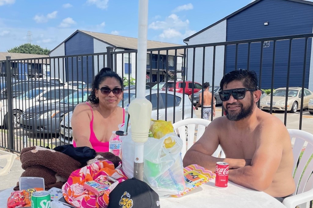A man and woman are sitting at a table with various items on it.
