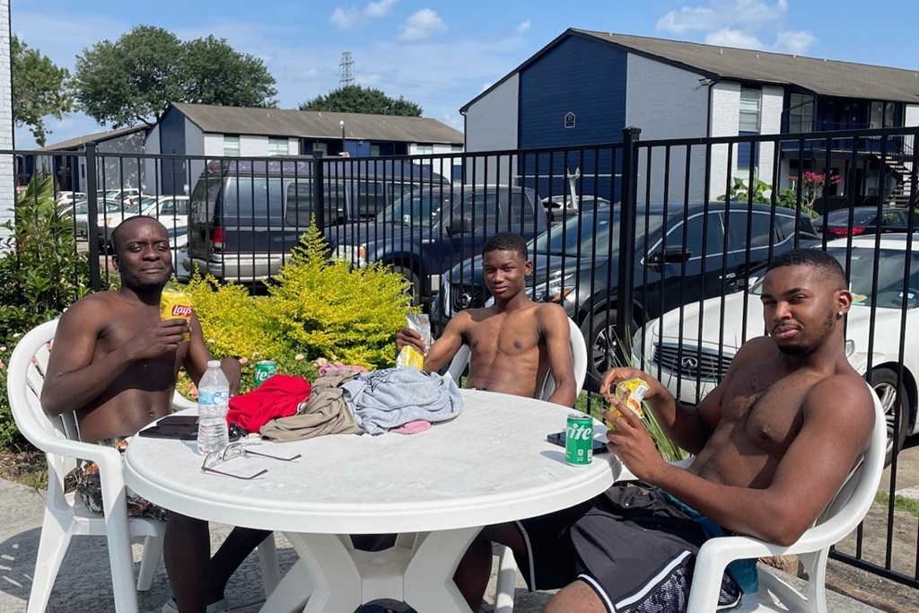 Three men are sitting at a table outside, eating and drinking.
