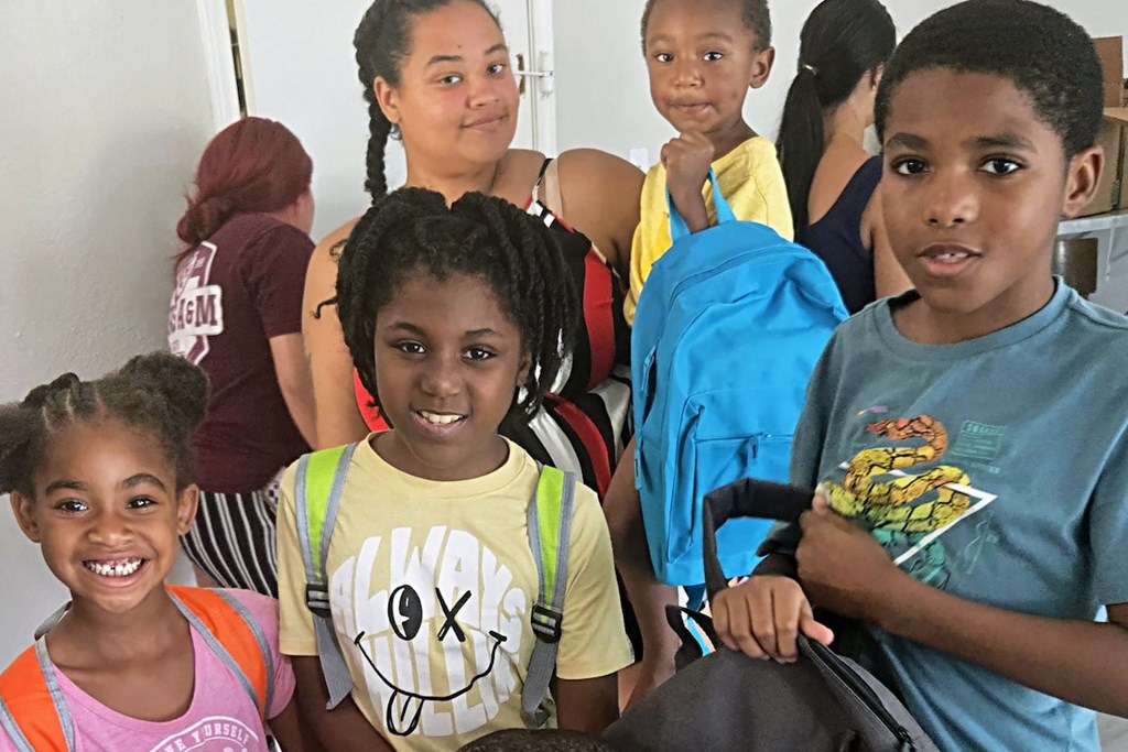 A group of children are standing together, some holding backpacks.