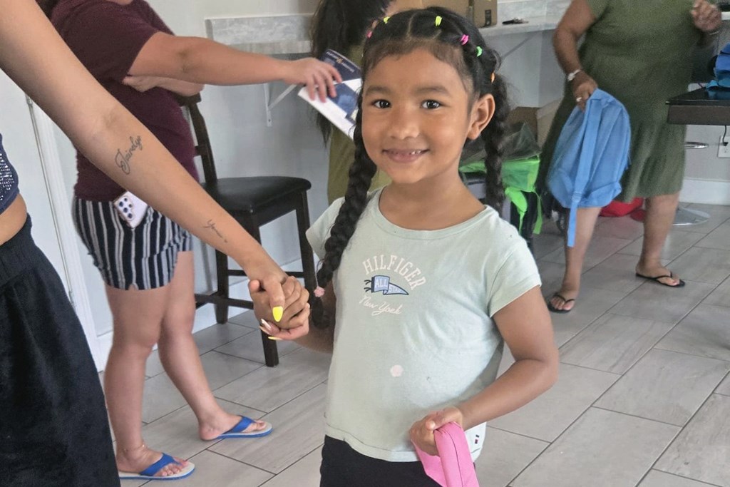 A young girl in a green shirt is holding a pink object.