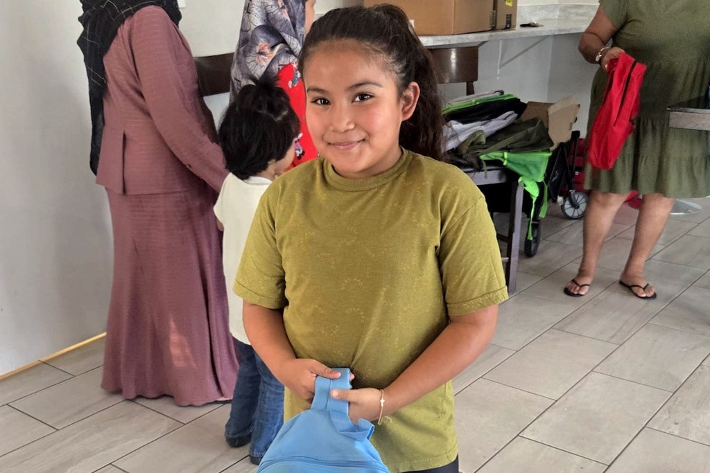 A girl in a green shirt is holding a blue bag.